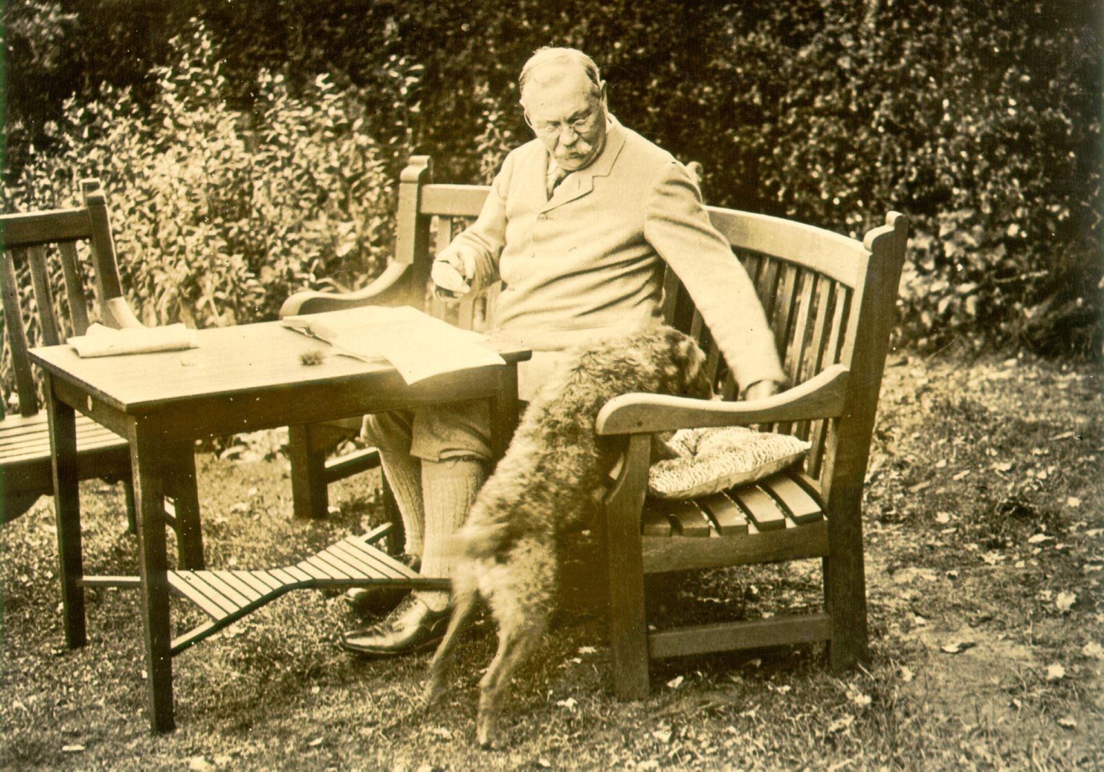 A photograph of Conan Doyle sitting on a bench with his dog